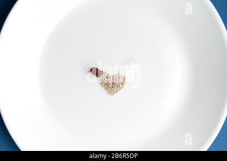 Granulate aus einer Kapsel auf eine weiße Platte in Form eines Herzens auf einem klassischen blauen Hintergrund gegossen. Das Herzsymbol besteht aus Granulat Stockfoto