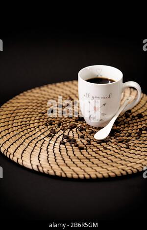 Weiße Keramikbecher mit den Worten "alles, was Sie brauchen, ist Liebe" voller schwarzer Kaffee auf einem Holztisch und Kaffeekörner Stockfoto