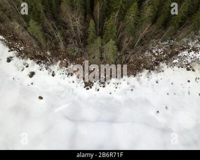 Luftaufnahme des flachen Ufers des zugefrorenen Sees durch Wald Stockfoto