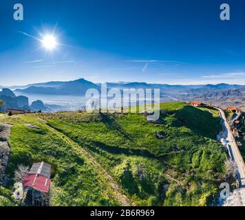Luftbild des Klosters des Wahrzeichen Canyons von Meteora und atemberaubendes malerisches Tal bei Sonnenuntergang, Schatten, verdrehte Straße, grüner Rasen Stockfoto