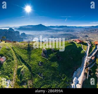Luftbild des Klosters des Wahrzeichen Canyons von Meteora und atemberaubendes malerisches Tal bei Sonnenuntergang, Schatten, verdrehte Straße, grüner Rasen Stockfoto