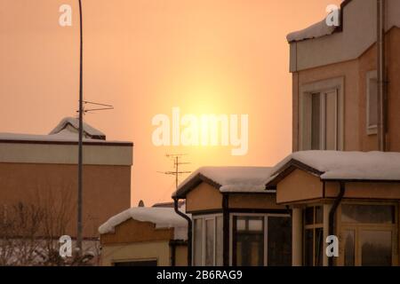 Sonnenaufgang und Wintermorgen in einem Hüttengebäude, gelbe Sonne und TV-Antenne, dunkle Flecken es ist starker Schnee, nicht Getreide oder Lärm, selektiver Fokus Stockfoto