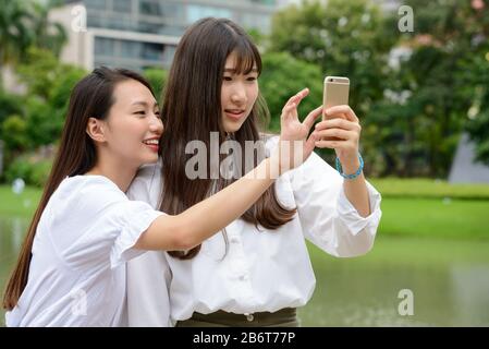 Zwei glückliche junge, schöne asiatische Teenager-Mädchen, die selfie im Park zusammen nehmen Stockfoto