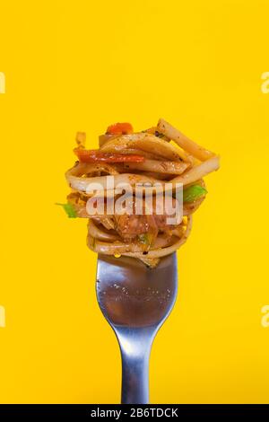 Klassische Spaghetticarbonara mit Hähnchenwunde auf Gabel auf lebhaftem gelbem Hintergrund. Spaghetti zu essen erfordert Gabel. Italienische Pasta und fast Food Takeawa Stockfoto