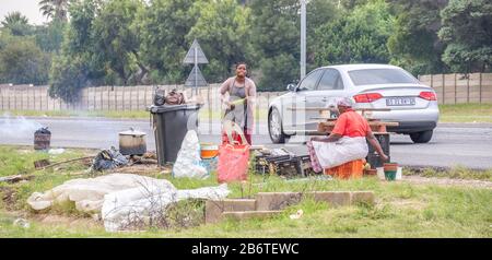 Alberton, Südafrika - unidentifizierte schwarze Afrikanerinnen verkaufen geröstete Mealies und frische Mangos aus einem provisorischen Straßenmeisterei Stockfoto