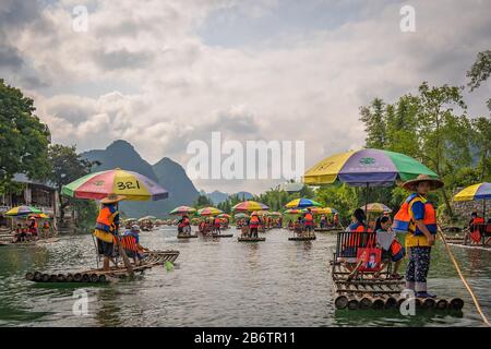 Yangshuo, China - August 2019: Touristen, die auf Bambusflößen sitzen, gelenkt von Führern mit langen Stöcken am malerischen und schönen Fluss Yulong Stockfoto