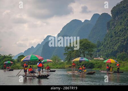 Yangshuo, China - August 2019: Touristen, die auf Bambusflößen sitzen, gelenkt von Führern mit langen Stöcken am malerischen und schönen Fluss Yulong Stockfoto