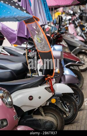 Yangshuo, China - August 2019: Reihe kleiner Motorräder und Roller, die auf einer Straße in der Yangshuo-Stadt in der Provinz Guangxi geparkt sind Stockfoto