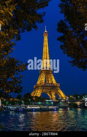 Beleuchteter Eiffelturm vor blauem Himmel. Wasser mit Spiegelung im Vordergrund. Stockfoto