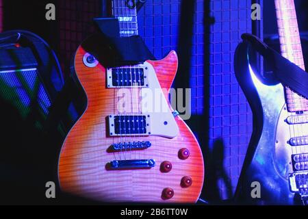 E-Gitarren stehen auf der Bühne auf Ständen unter dem Licht von Scheinwerfern. Stockfoto