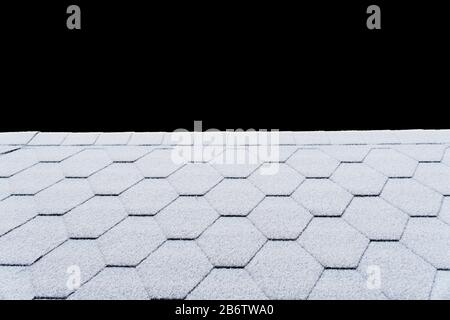 Asphalt Dachschindeln Textur bedeckt mit leichtem Schnee. Mit Frost bedeckte Hausdachschindeln. Schneebedecktes Dach des Hauses isoliert auf schwarzem Bac Stockfoto