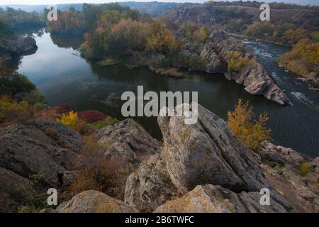 Malerische Flussbiegung in der Herbstsaison. Berühmter integraler Riffel des südlichen Flusses Bug. Felsen und hochfarbige Bäume im Vordergrund. Stockfoto