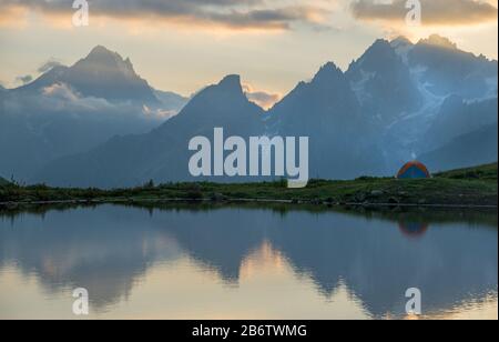 Buntes Camp (Zelt) in der Nähe des Bergsees. Sonnenuntergangsszene im Hintergrund. Stockfoto