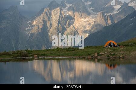 Touristen mit Camp (Zelt) in der Nähe des Bergsees. Felsen mit Schnee im Hintergrund. Stockfoto