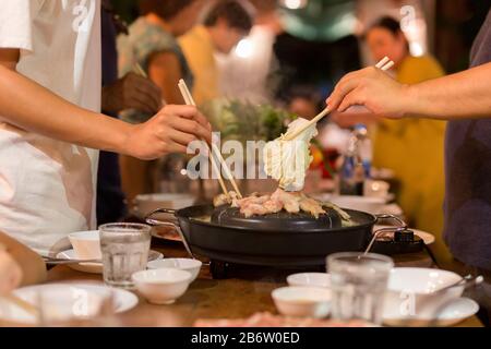 Hand mit Essstäbchen, grillfleisch, Schweinefleisch und Vegeteble beim Familienessen. Stockfoto