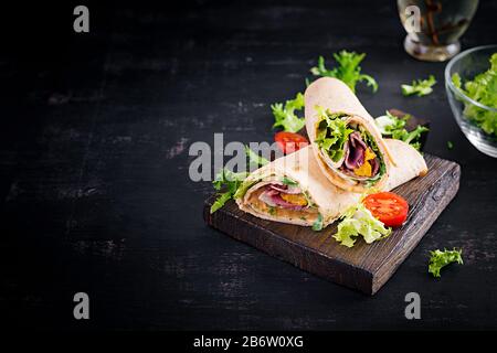 Frische Tortilla-Wraps mit Schinkenbeef und frischem Gemüse auf Holzbrett. Rinderburrito. Mexikanische Küche. Kopierbereich Stockfoto