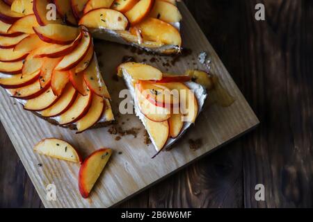 Hausgemachter Käsekuchen mit Pfirsichen. Gesundes Fruchtdessert mit Frischkäse, Nektarinen, Honig und Thymian auf Holzbrett. Diät-Kuchen Stockfoto