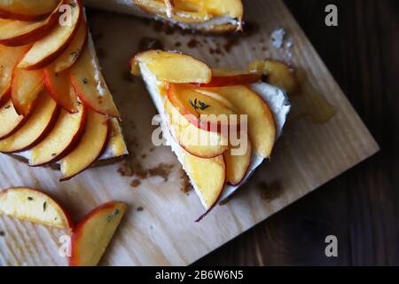 Hausgemachter Käsekuchen mit Pfirsichen. Gesundes Fruchtdessert mit Frischkäse, Nektarinen, Honig und Thymian auf Holzbrett. Diät-Kuchen Stockfoto