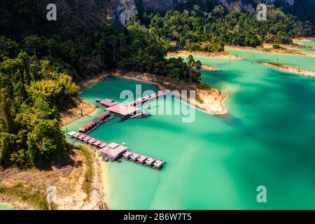 Luftdronblick auf ein schwimmendes Holzsparren, umgeben von riesigen Klippen und tropischem Dschungel (Khao Sok) Stockfoto