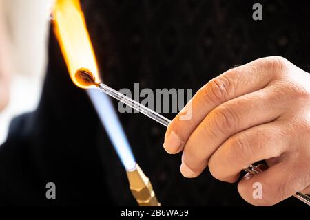 Die Hände des Handwerkers, der ein Glasthema des Handwerks macht. Glashersteller arbeiten geschmolzenes Glas mit einer flammenden Fackel. Nahaufnahme der Flamme von der Blasbrenner Stockfoto