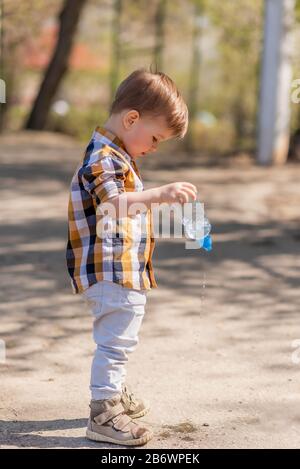 Das schöne Kind gießt Wasser aus einer Flasche auf dem Straßenbelag Stockfoto