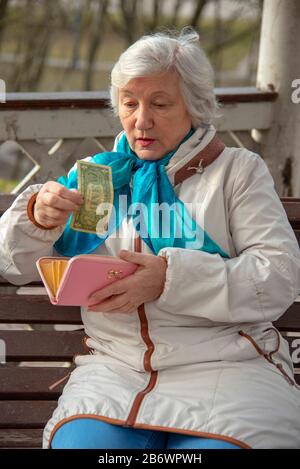 Ein trauriger Rentner von 70 Jahren sitzt auf einer Parkbank und zählt das Geld in ihrer Brieftasche. Stockfoto