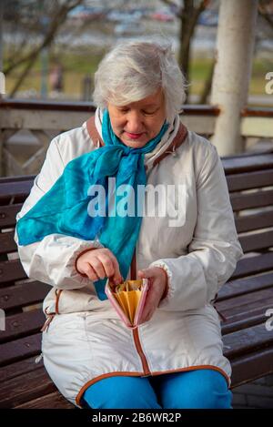 Ein trauriger Rentner von 70 Jahren sitzt auf einer Parkbank und zählt das Geld in ihrer Brieftasche. Stockfoto