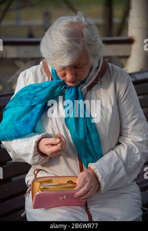 Ein trauriger Rentner von 70 Jahren sitzt auf einer Parkbank und zählt das Geld in ihrer Brieftasche. Stockfoto