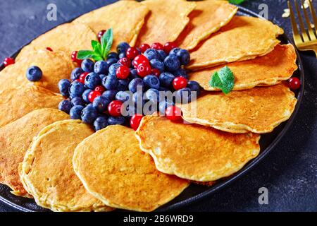 Haferbrei Pfannkuchen serviert mit frischen Blaubeeren und Preiselbeeren auf einer schwarzen Platte, horizontaler Blick von oben, aus der Nähe Stockfoto