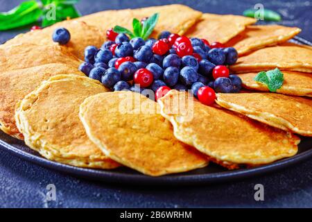 Nahaufnahme von Haferflocht-Pfannkuchen mit frischen Blaubeeren und Preiselbeeren auf einer schwarzen Platte Stockfoto