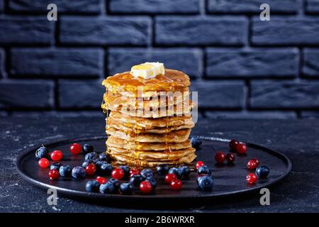 Haferbrei Pfannkuchen mit Butter und geschmolzenem Honig auf einem Teller mit Beeren. Backstein im Hintergrund, Nahaufnahme Stockfoto