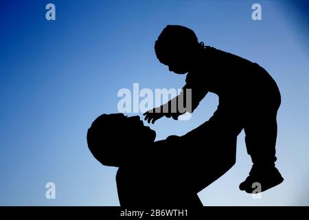 Silhouetten von Vater und Sohn, die vor dem blauen Himmel spielen. Konzept Sommerurlaub, liebevolle und freundliche Familie. Stockfoto