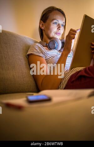 Hübsche, junge Frau, die zu Hause in den Abend arbeiten - mit Ihren Tablet-PC sowie Bluetooth® Kopfhörer, schreiben Sie einige Ideen für morgen Stockfoto
