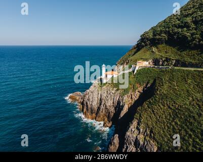 Luftaufnahme von Klippe mit Leuchtturm auf der Kante und dem Ozean, der auf die Felsen trifft Stockfoto