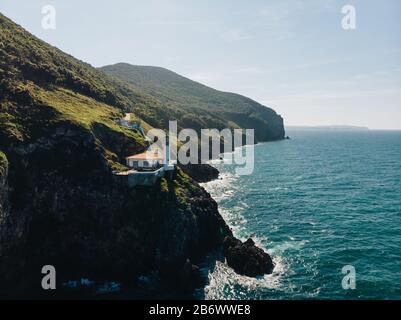 Luftaufnahme von Klippe mit Leuchtturm auf der Kante und dem Ozean, der auf die Felsen trifft Stockfoto