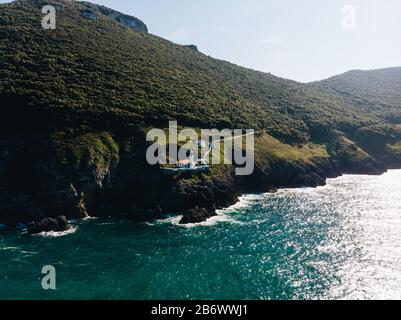 Luftaufnahme von Klippe mit Leuchtturm auf der Kante und dem Ozean, der auf die Felsen trifft Stockfoto