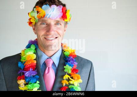 Fröhlicher Geschäftsmann lächelnd mit farbenfroher Blumenkette und Stirnband Stockfoto