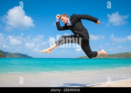 Aufgeregter Geschäftsmann springt barfuß in seinem Anzug über einen leeren tropischen Strand Stockfoto