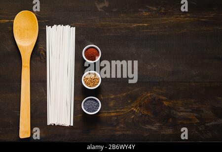 Verschiedene Gewürze und rohe Eudon Nudeln auf dunklem Hintergrund. Stockfoto