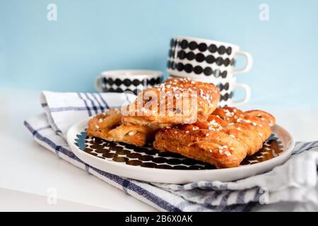 Frühstückseinrichtung mit dänischem Gebäck und Kaffeetassen, die auf weichem, blauem Hintergrund gefüllt werden können. Stockfoto