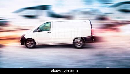 Weißer Lieferwagen, der auf der Straße mit verschwommenem Hintergrund beschleunigt. Stockfoto