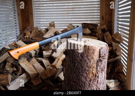 Nahaufnahme der Axt, die zum Schneiden von Protokollen bereit ist. Holzschnitt im Schuppenkonzept. Bereits gehackte Brennholzverlegung im Hintergrund. Stockfoto