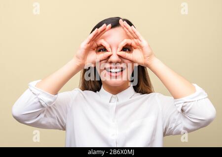 Sehhilfen: Junge Frau hält ihre Hände über ihre Augen und imitiert Brille und lächelt fröhlich Stockfoto