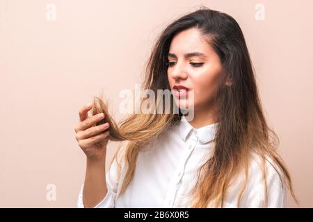 Haarprobleme: Junge Frau in weißem Hemd, die ihre Brülle, beschädigte und gespaltene Haare vor rosa Hintergrund überprüft Stockfoto