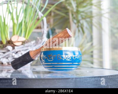 Haulerwijk - 07. märz 2020: Haulerwijk, Niederlande. Blaue und goldene indische Gesangsschale aus sieben Metallen mit einem Holzstreifer auf einem Glas Stockfoto