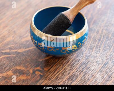 Haulerwijk - 07. März 2020: Haulerwijk, Niederlande. Blaue und goldene indische Gesangsschüssel aus sieben Metallen mit einem Holzstreifer auf einem Holz Stockfoto