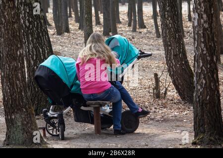 Frau mit einem Kinderwagen für Zwillinge auf einem Spaziergang im Park. Menschen Stockfoto