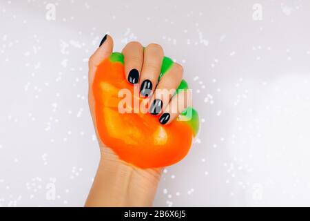 Hände mit schwarzer Maniküre, die Schleim in orange und grün leuchtenden Farben hält Stockfoto