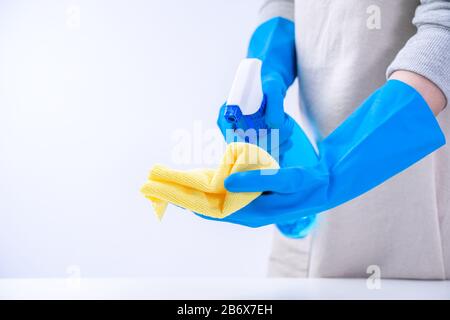 Die Haushälterin der jungen Frau putzt den weißen Tisch in der Schürze mit blauen Handschuhen, Spritzreiniger, nassem gelbem Lappen, Nahaufnahme, Kopierraum, leerer Designkon Stockfoto