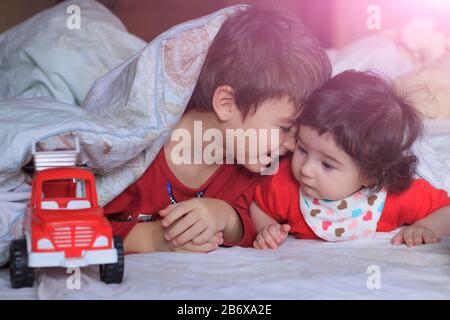 Zwei Kinder in roter Kleidung liegen lächelnd unter einer Lichtdecke. Davor steht ein spielzeugrotes Auto. Nahaufnahme Stockfoto